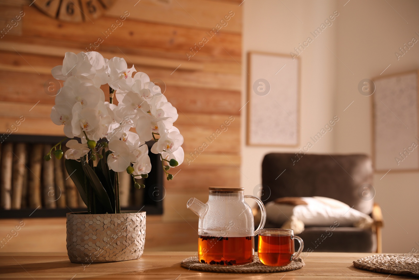 Photo of Beautiful orchid, teapot and cup with hot tea on table indoors