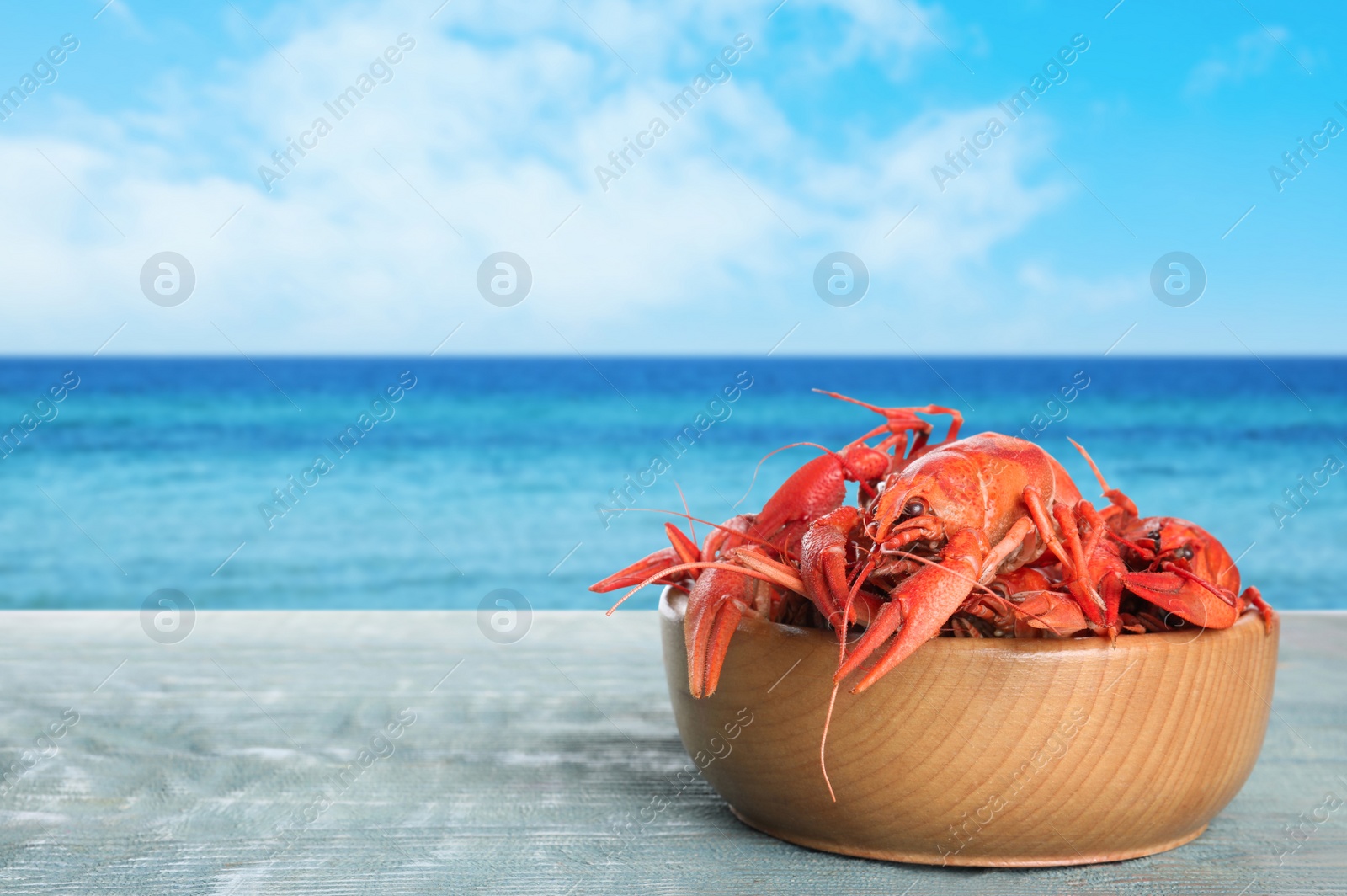 Image of Cooked crayfishes on wooden table near sea. Space for text