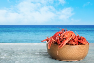 Image of Cooked crayfishes on wooden table near sea. Space for text