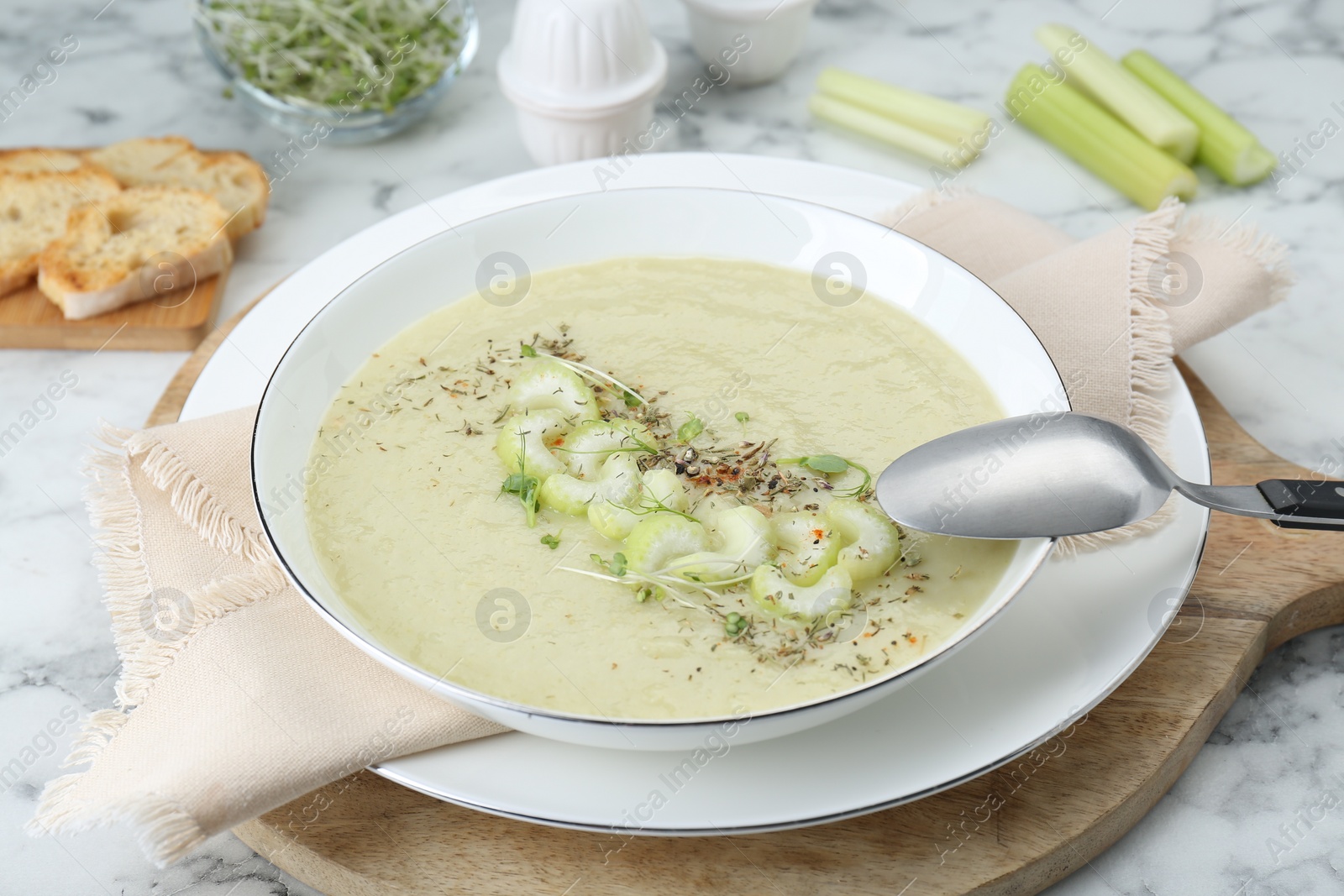 Photo of Bowl of delicious celery soup and spoon on white table, closeup