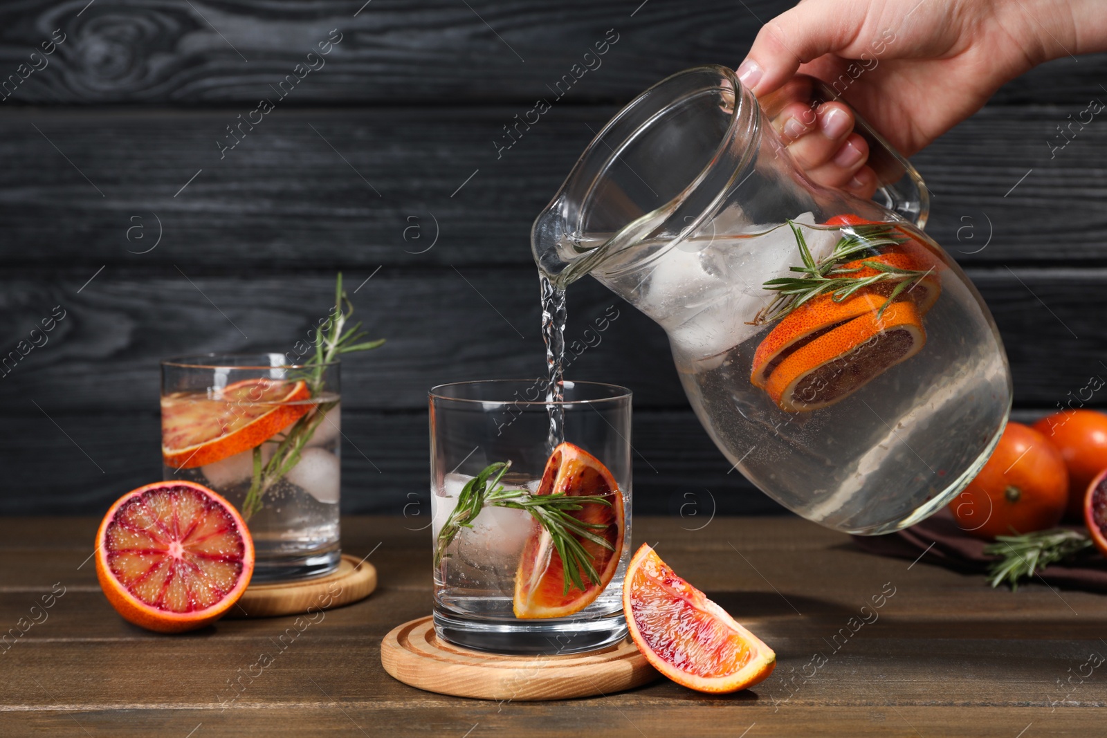 Photo of Woman pouring refreshing drink with sicilian orange from jug into glass at wooden table, closeup