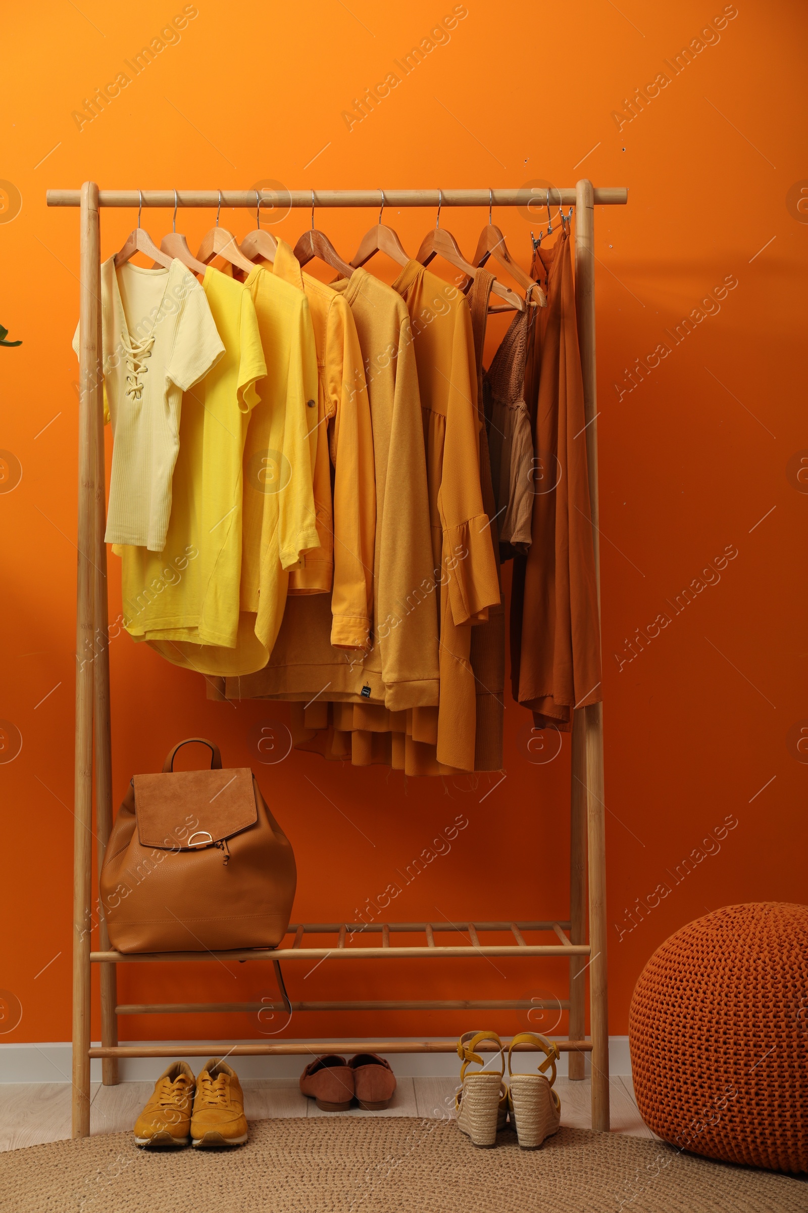 Photo of Rack with different stylish women`s clothes, shoes, backpack and pouf near orange wall indoors