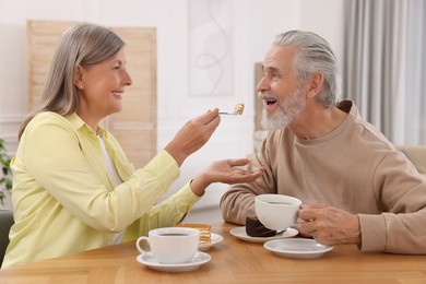 Photo of Affectionate senior couple having breakfast at wooden table in room