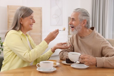 Affectionate senior couple having breakfast at wooden table in room