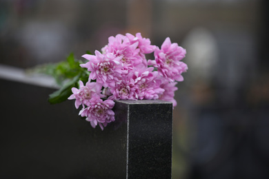 Photo of Chrysanthemum flowers on black granite tombstone outdoors. Funeral ceremony