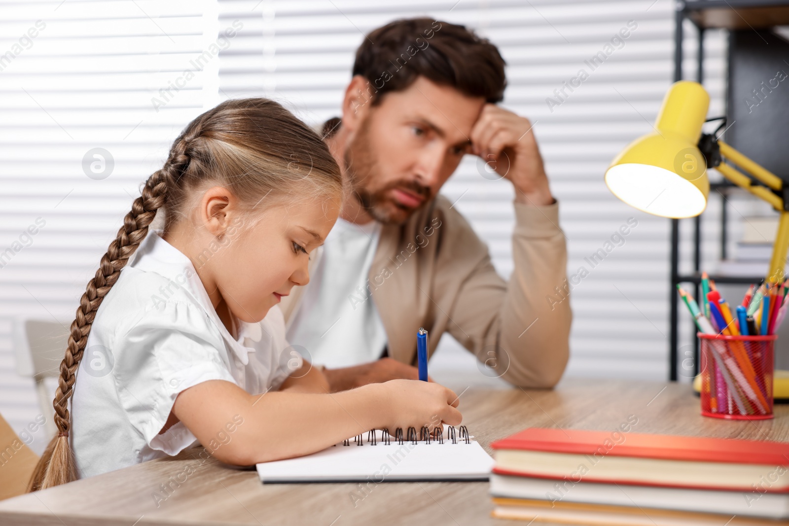 Photo of Dyslexia problem. Annoyed father helping daughter with homework at table indoors, selective focus