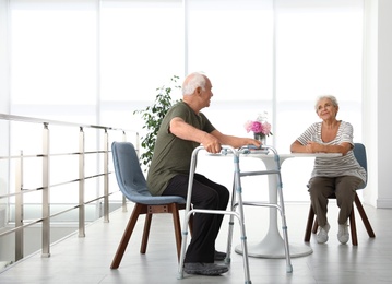 Photo of Elderly woman and her husband with walking frame indoors