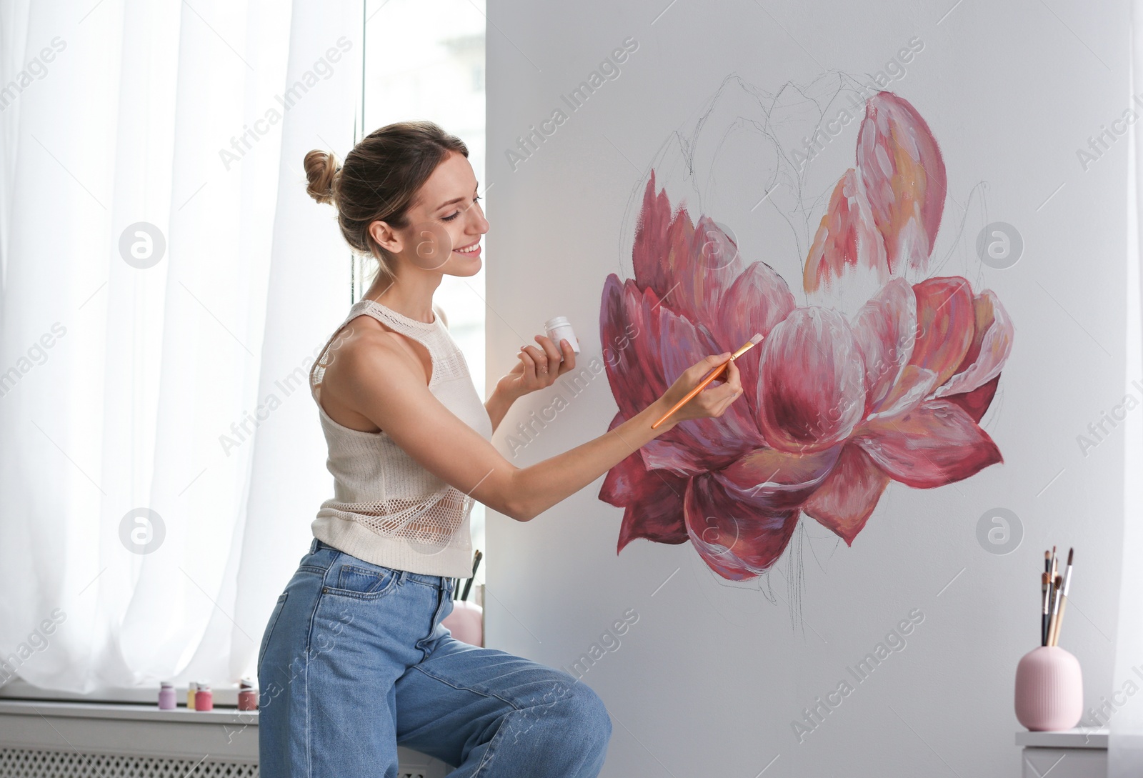 Photo of Decorator painting flower on white wall in room. Interior design