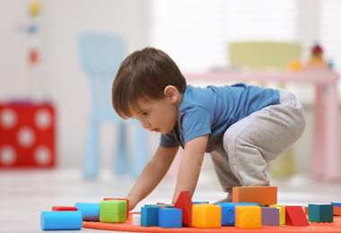 Photo of Cute little child playing with toy blocks on floor at home