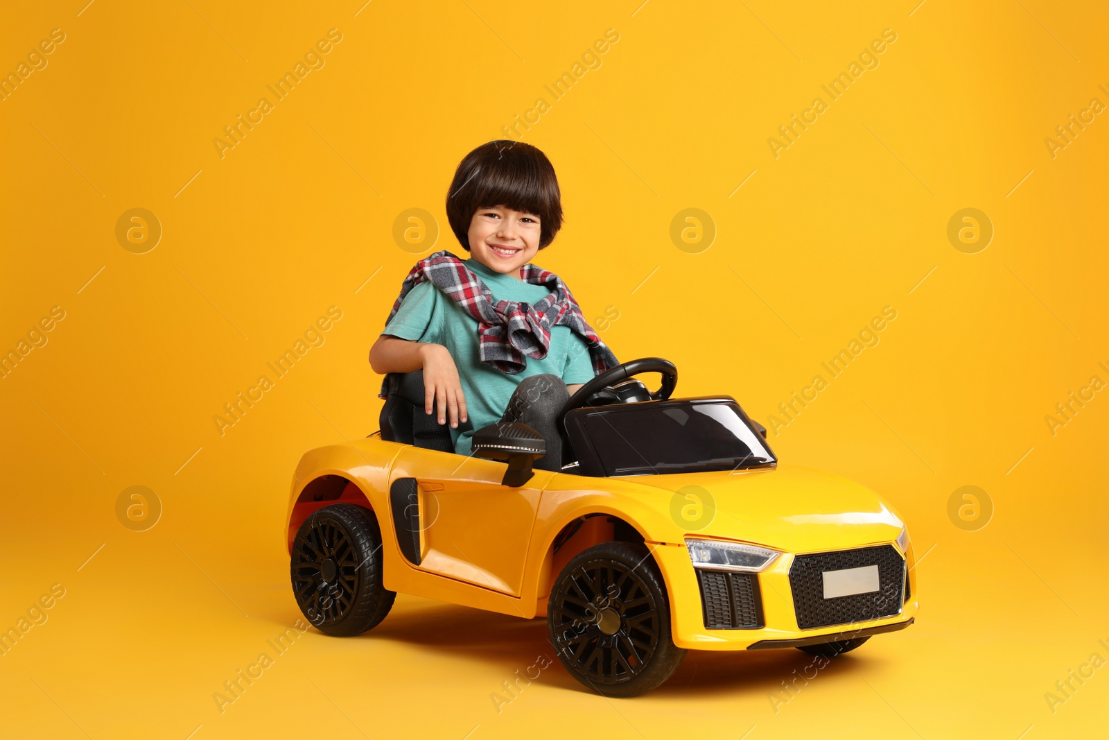 Photo of Little child driving toy car on yellow background