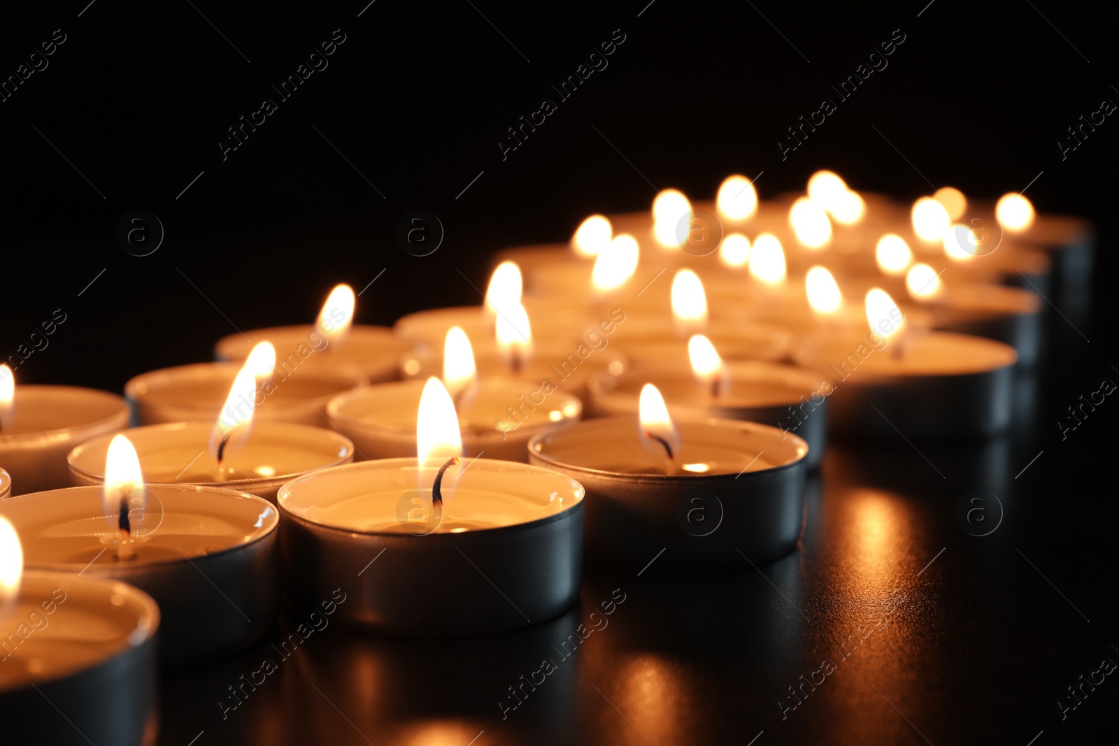 Photo of Wax candles burning on table in darkness, closeup