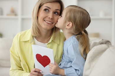 Photo of Little daughter kissing and congratulating her mom with greeting card at home. Happy Mother's Day