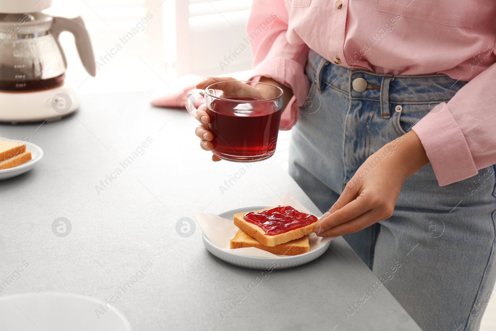 Photo of Woman having tasty breakfast with toast and raspberry tea at home, closeup. Morning routine