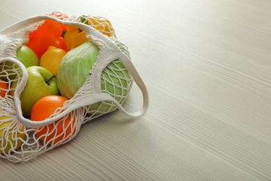 Photo of Net bag with vegetables and fruits on wooden table. Space for text