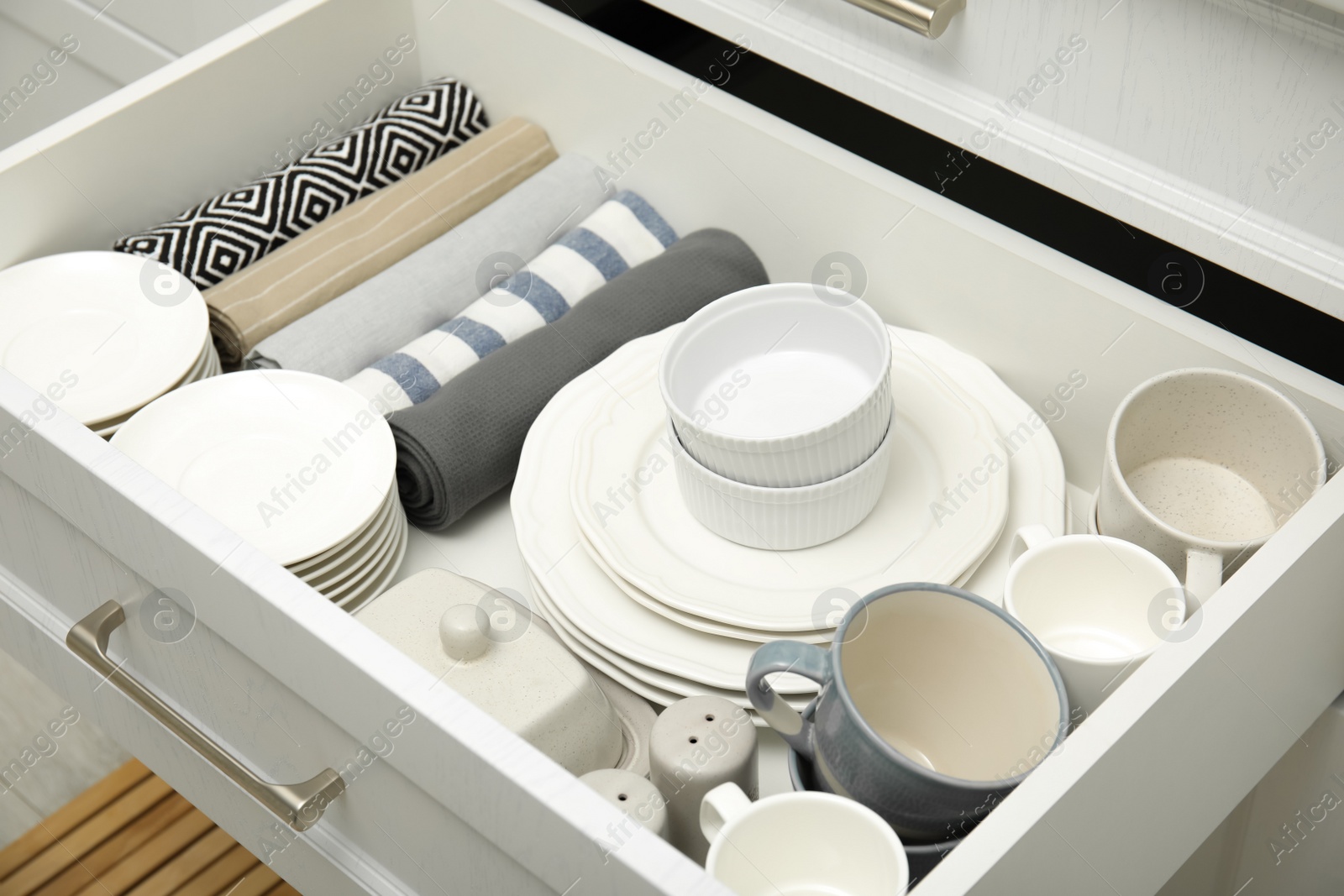 Photo of Open drawer of kitchen cabinet with different dishware and towels