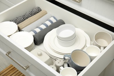 Open drawer of kitchen cabinet with different dishware and towels