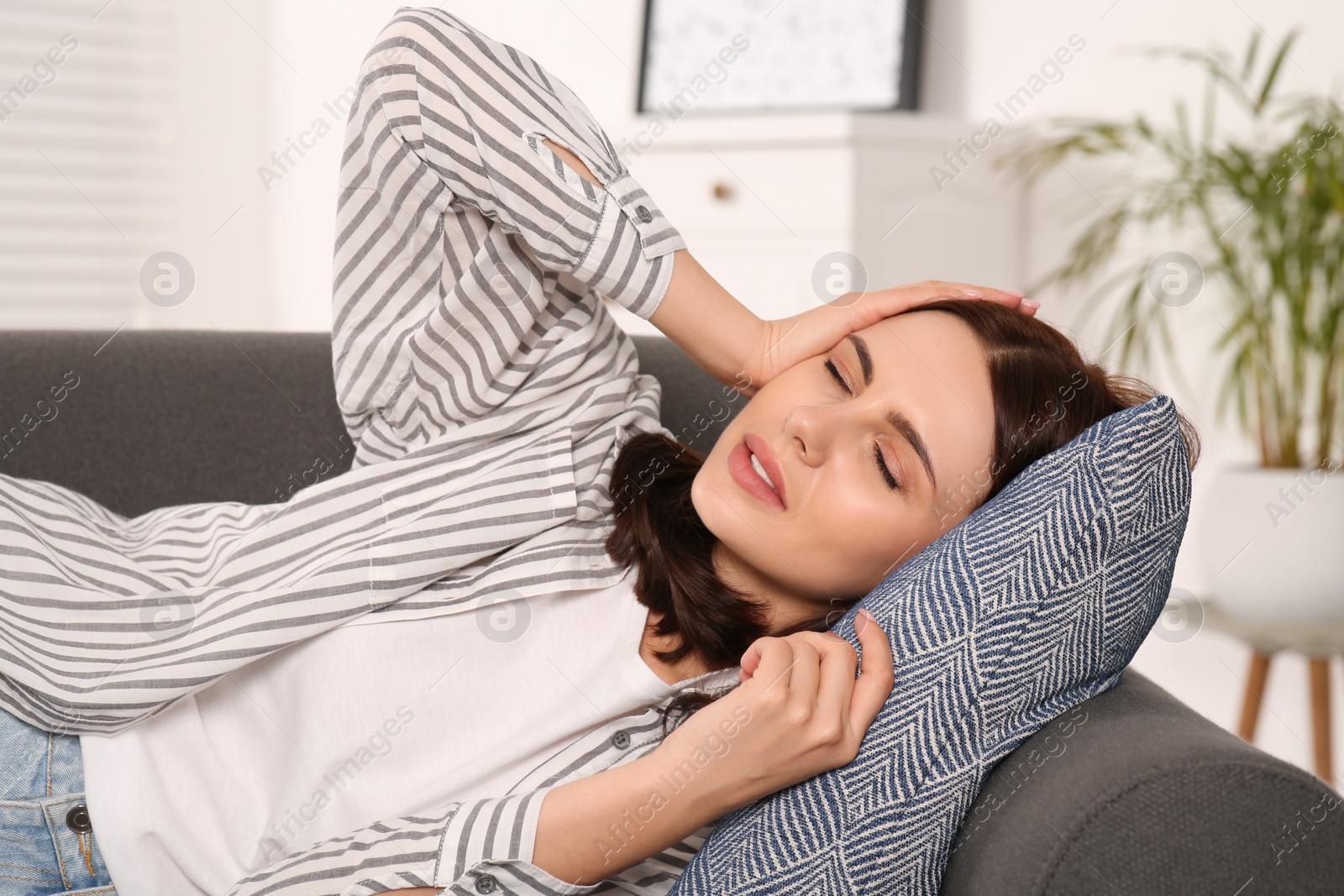 Photo of Young woman suffering from headache on sofa indoors. Hormonal disorders