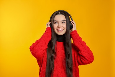Photo of Teenage girl listening music with headphones on yellow background