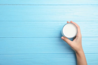 Woman holding glass of milk on wooden table, top view. Space for text