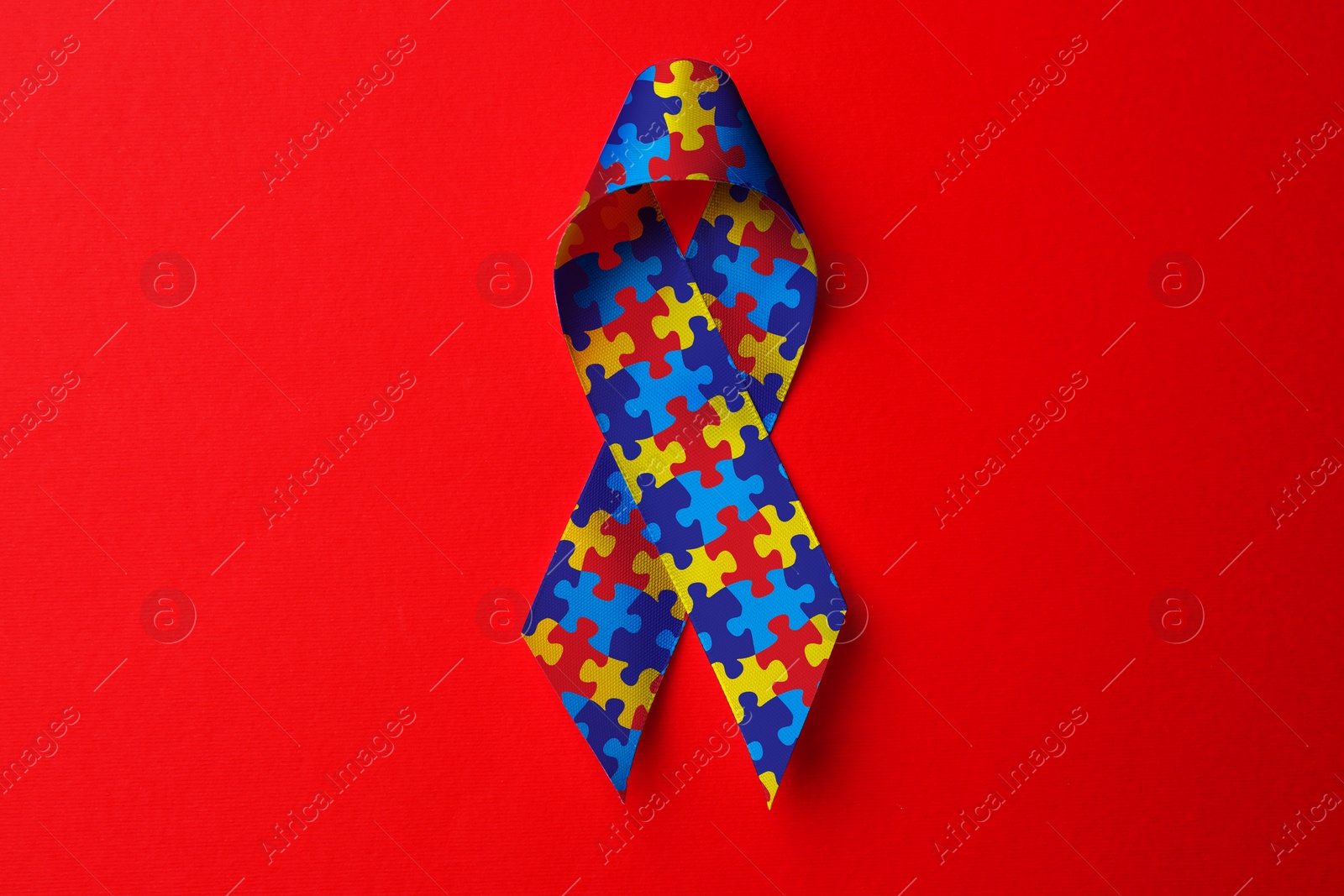 Image of World Autism Awareness Day. Colorful puzzle ribbon on red background, top view