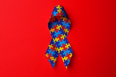Image of World Autism Awareness Day. Colorful puzzle ribbon on red background, top view