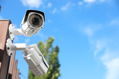 Photo of Modern CCTV security cameras against blue sky. Space for text