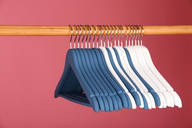 Photo of Empty clothes hangers on wooden rail against color background