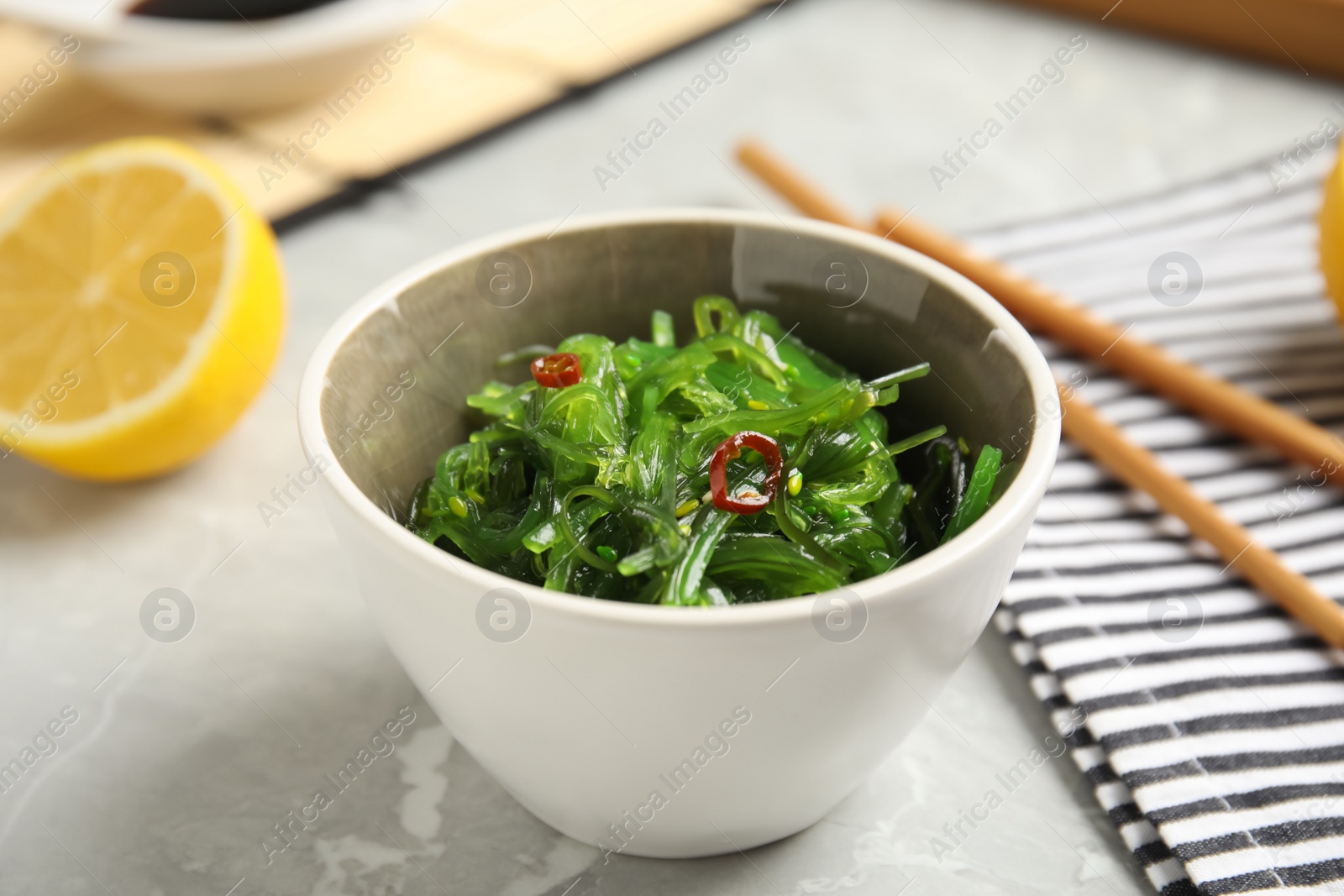 Photo of Japanese seaweed salad served on light marble table, closeup