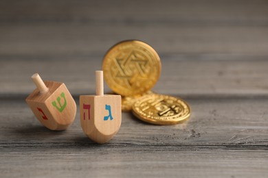 Dreidels with Jewish letters and coins on wooden table, space for text. Traditional Hanukkah game