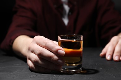 Photo of Alcohol addiction. Woman with glass of whiskey at dark textured table, selective focus