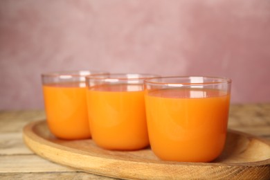 Photo of Glasses of freshly made carrot juice on wooden plate
