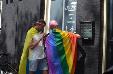 Photo of AMSTERDAM, NETHERLANDS - AUGUST 06, 2022: Men with LGBT pride flags on city street