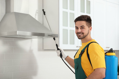 Photo of Pest control worker spraying insecticide on furniture in kitchen