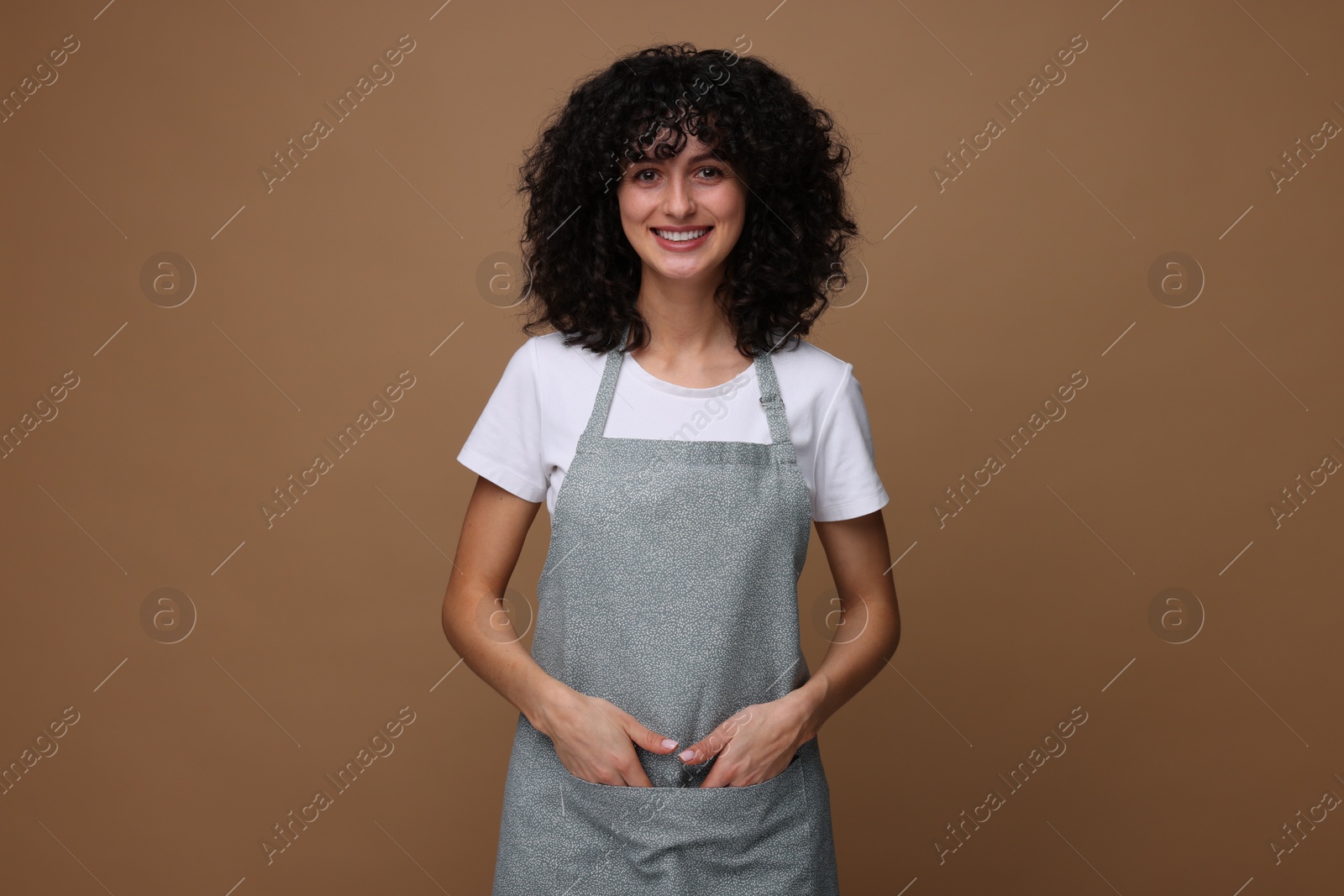 Photo of Happy woman wearing kitchen apron on brown background. Mockup for design