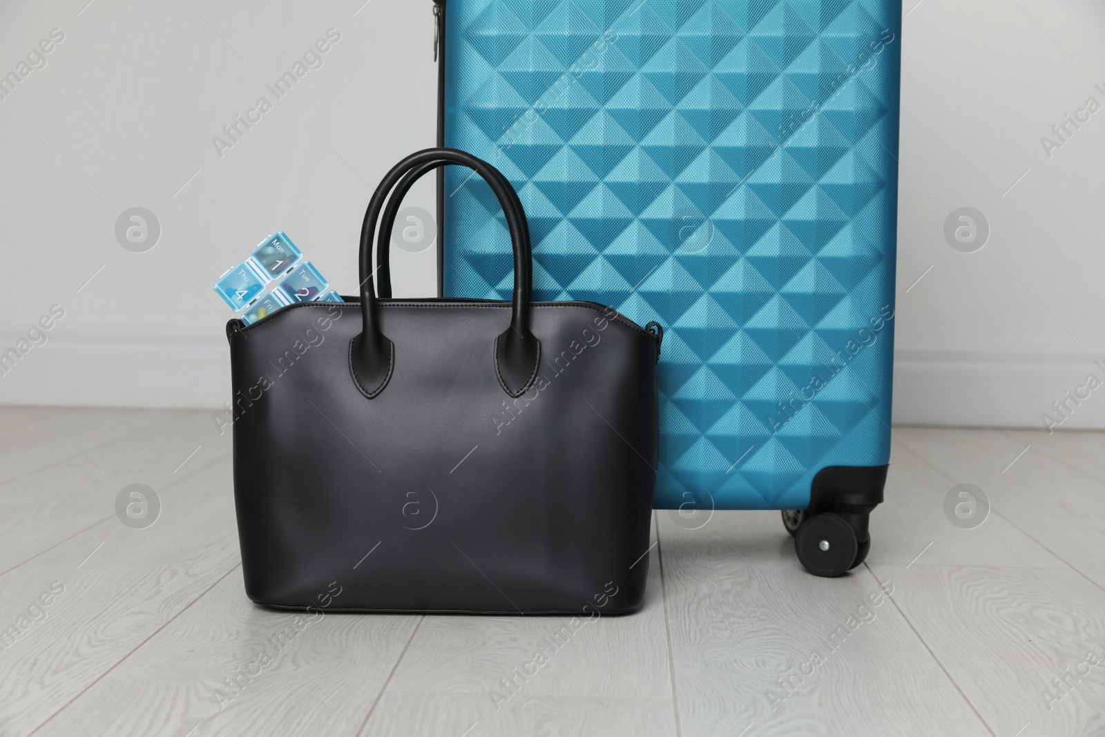 Photo of Stylish bag with pill box near suitcase on floor indoors