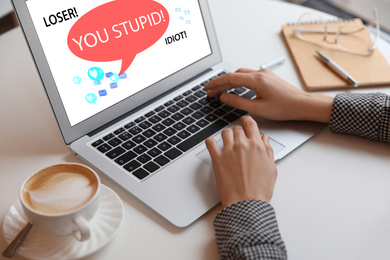 Young woman using laptop at white table, closeup. Cyber bullying