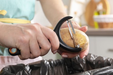 Woman peeling fresh potato above garbage bin indoors, closeup