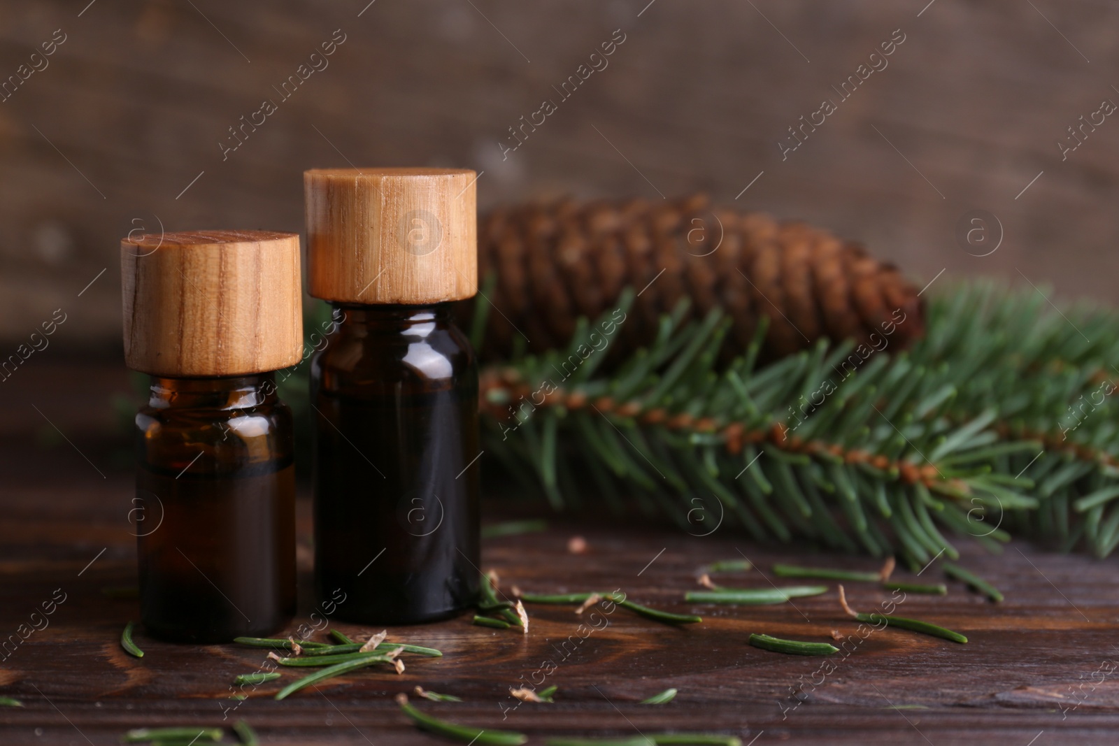 Photo of Bottles of aromatic essential oil, pine branches and cone on wooden table, closeup