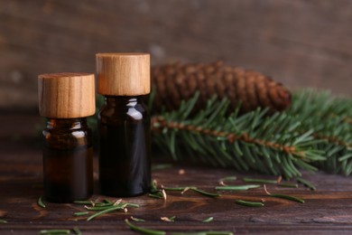 Photo of Bottles of aromatic essential oil, pine branches and cone on wooden table, closeup