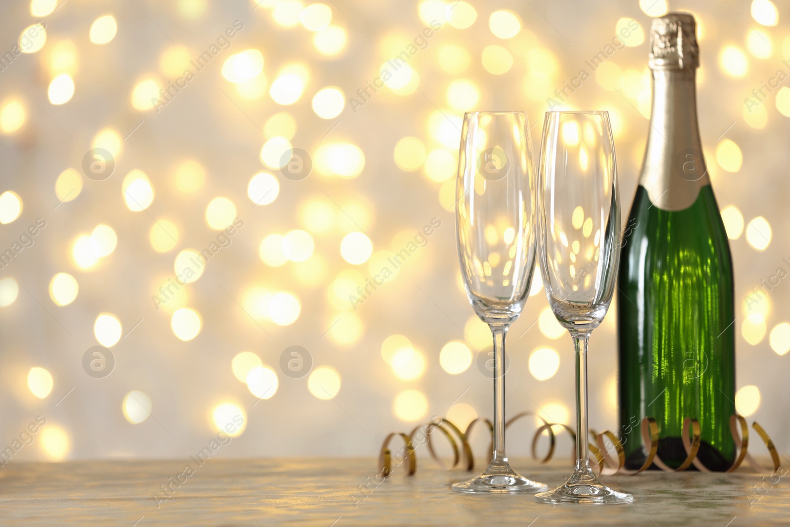 Photo of Empty glasses and bottle of champagne on table against blurred lights. Space for text