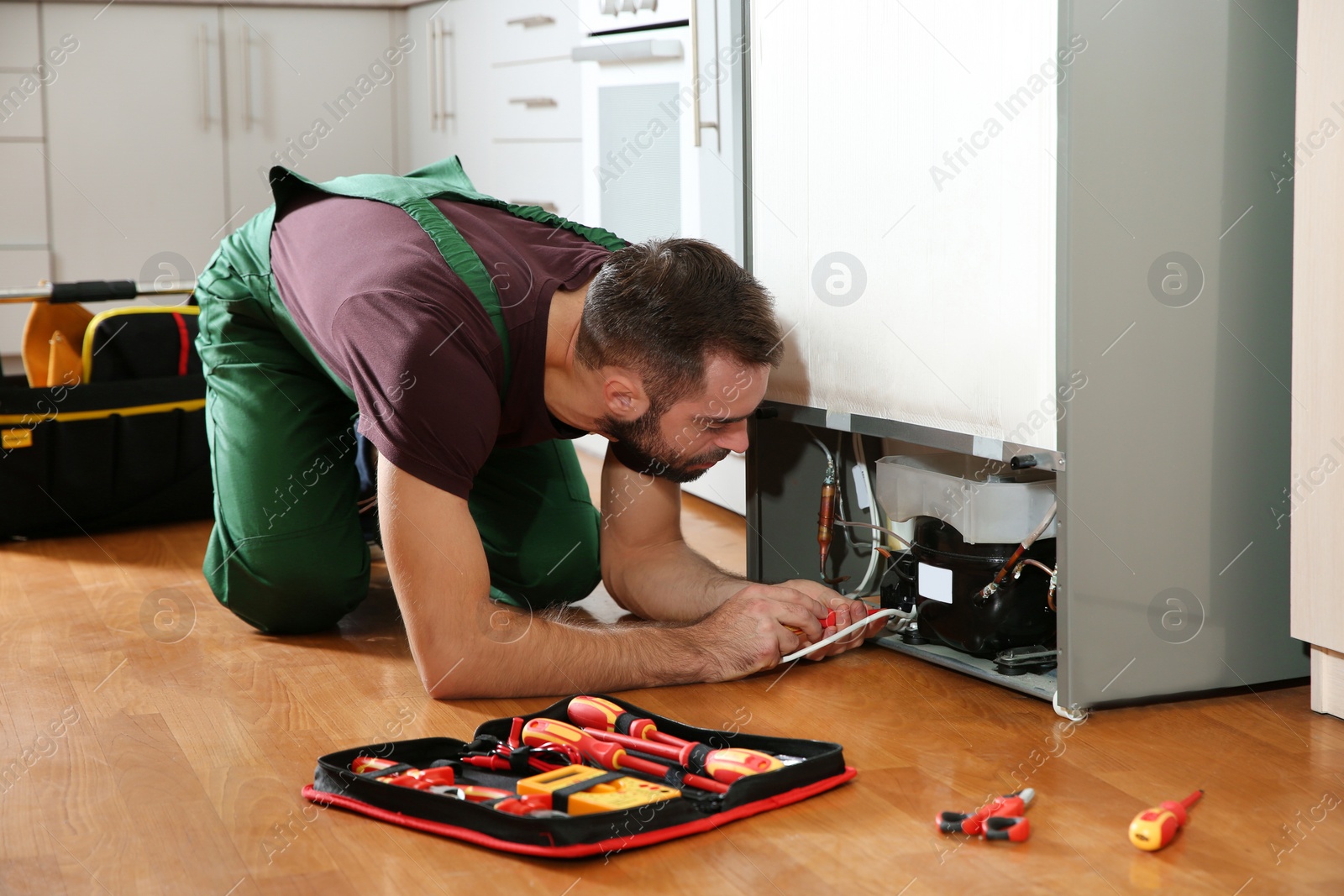 Photo of Male technician in uniform repairing refrigerator indoors