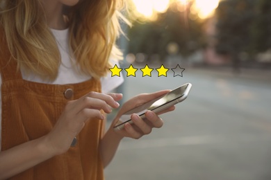 Image of Woman leaving review online via smartphone outdoors, closeup. Four out of five stars over gadget