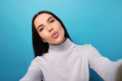 Photo of Beautiful young woman taking selfie while blowing kiss on light blue background