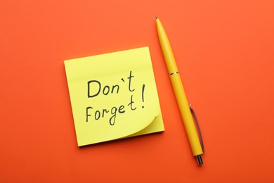 Photo of Paper note with phrase Don't Forget and pen on orange background, flat lay