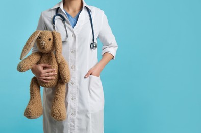Photo of Pediatrician with toy bunny and stethoscope on turquoise background, closeup. Space for text