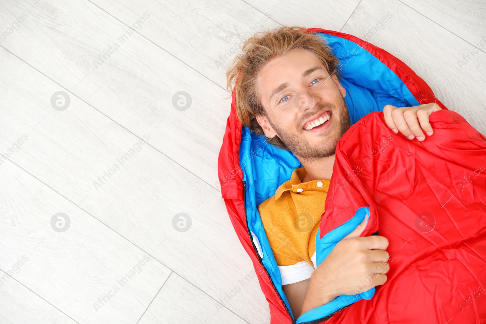 Photo of Young man in comfortable sleeping bag on floor, top view. Space for text