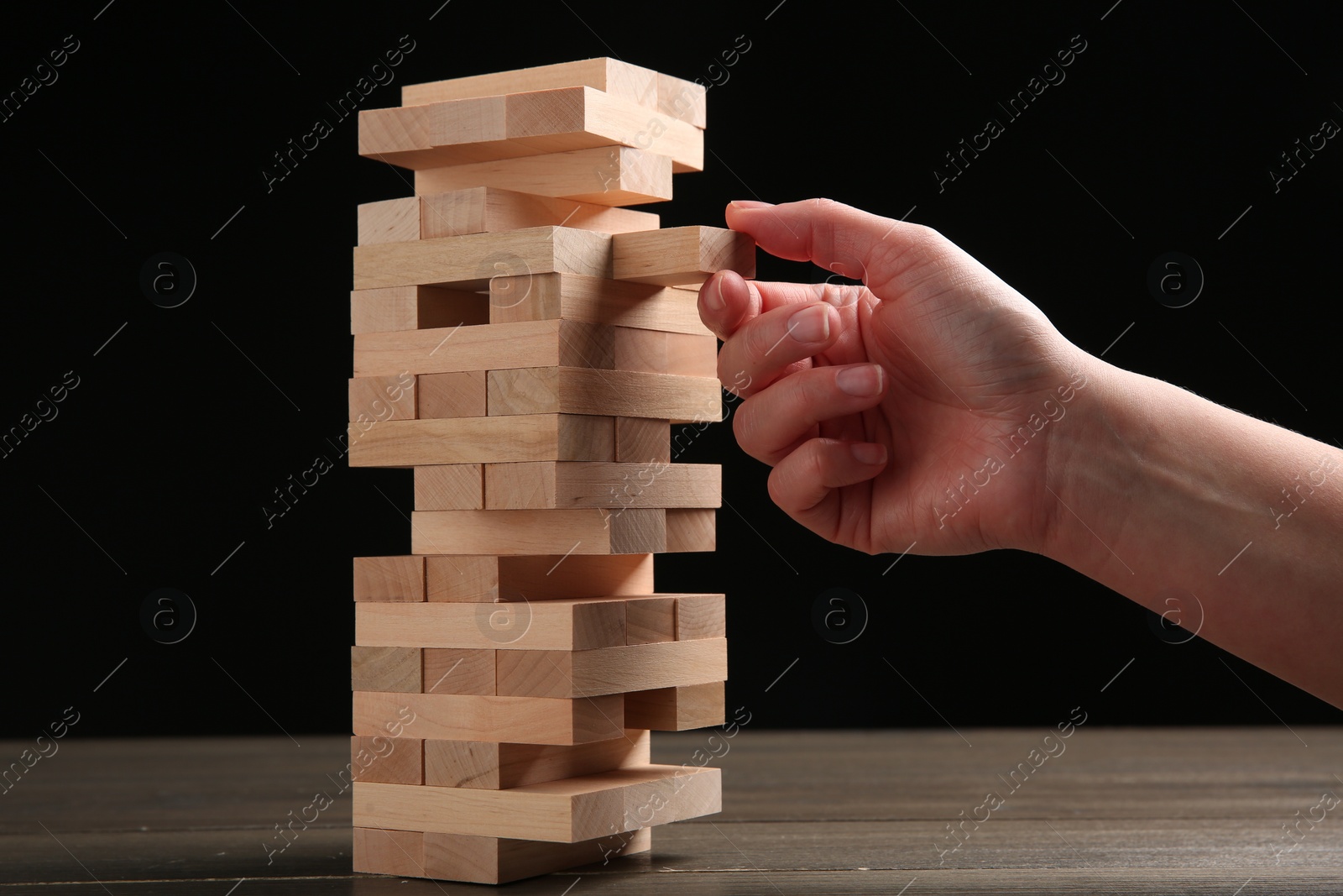 Photo of Woman playing Jenga at table against black background, closeup