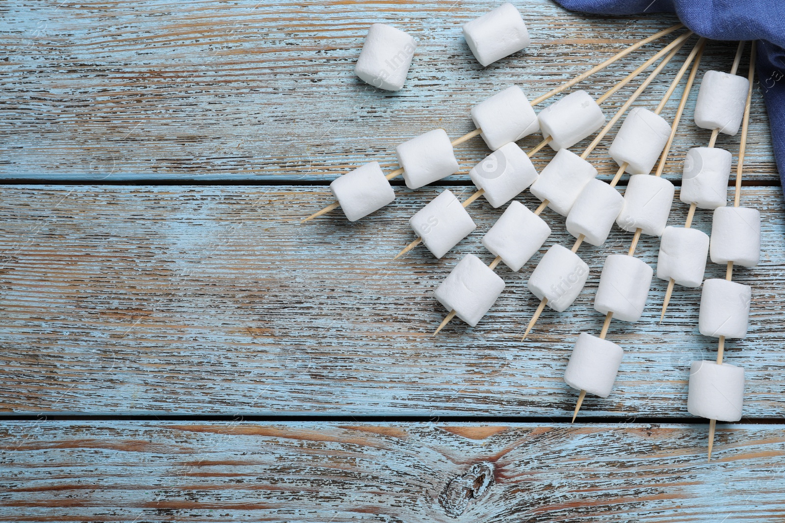 Photo of Sticks with delicious puffy marshmallows on light blue wooden table, flat lay. Space for text