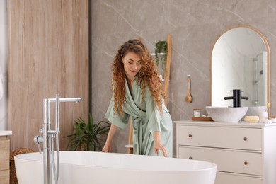 Photo of Beautiful woman in green silk robe near bathtub at home