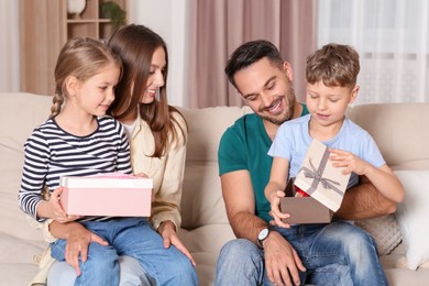 Photo of Happy family presenting each other with gifts on sofa at home